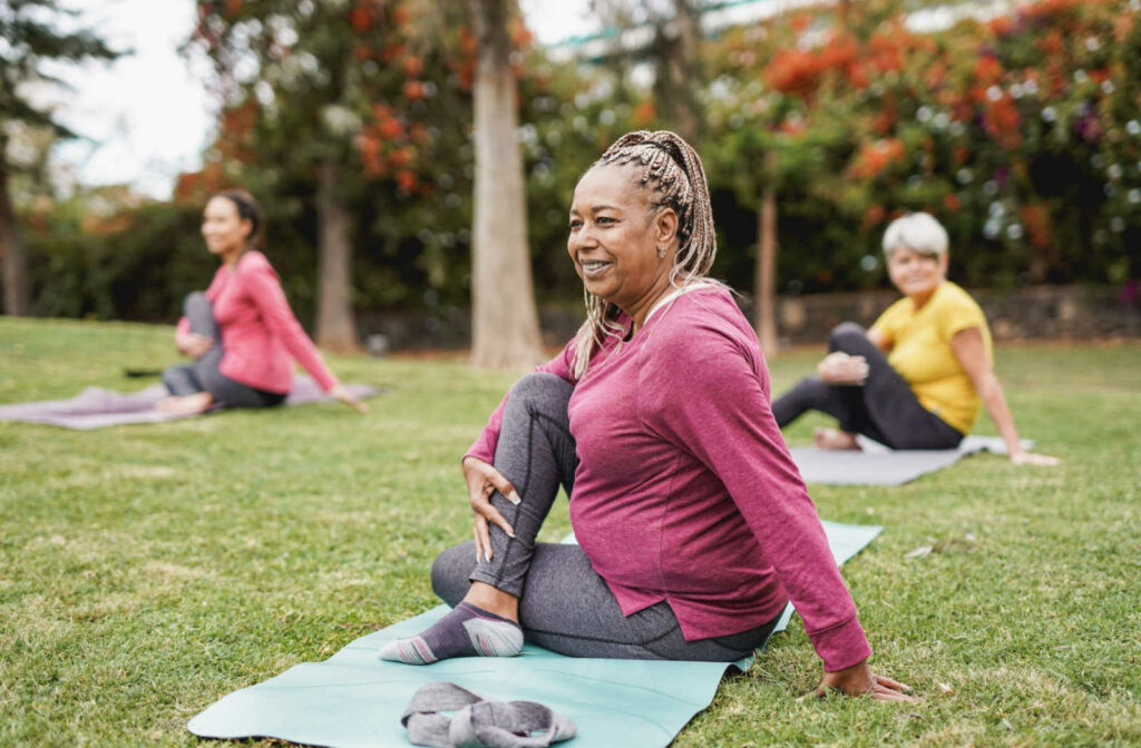 A group of older women doing yoga together in a park or outdoor setting, promoting social inclusivity and body positivity.