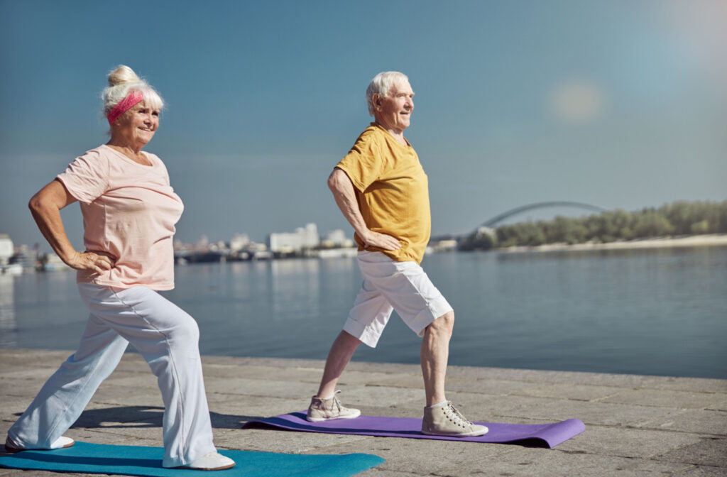 An older adult woman and an older adult man standing on a yoga mat and doing hip exercise.