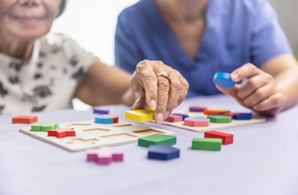 An older adult woman solving a puzzle with the assistance of a memory care staff.