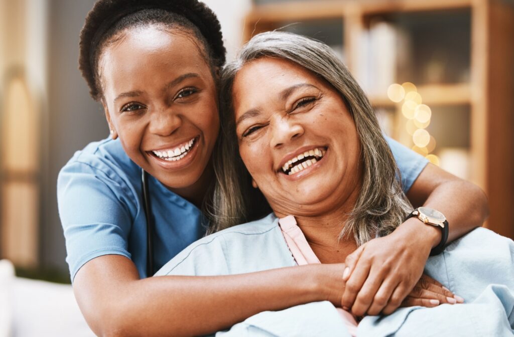 A caregiver assisting an older adult seated on the edge of a bed in a bright, cozy room.