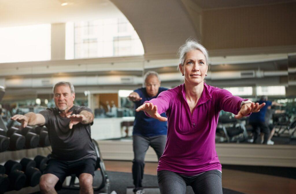 A group of three older adults performing squats in a gym as a form of occupational therapy.