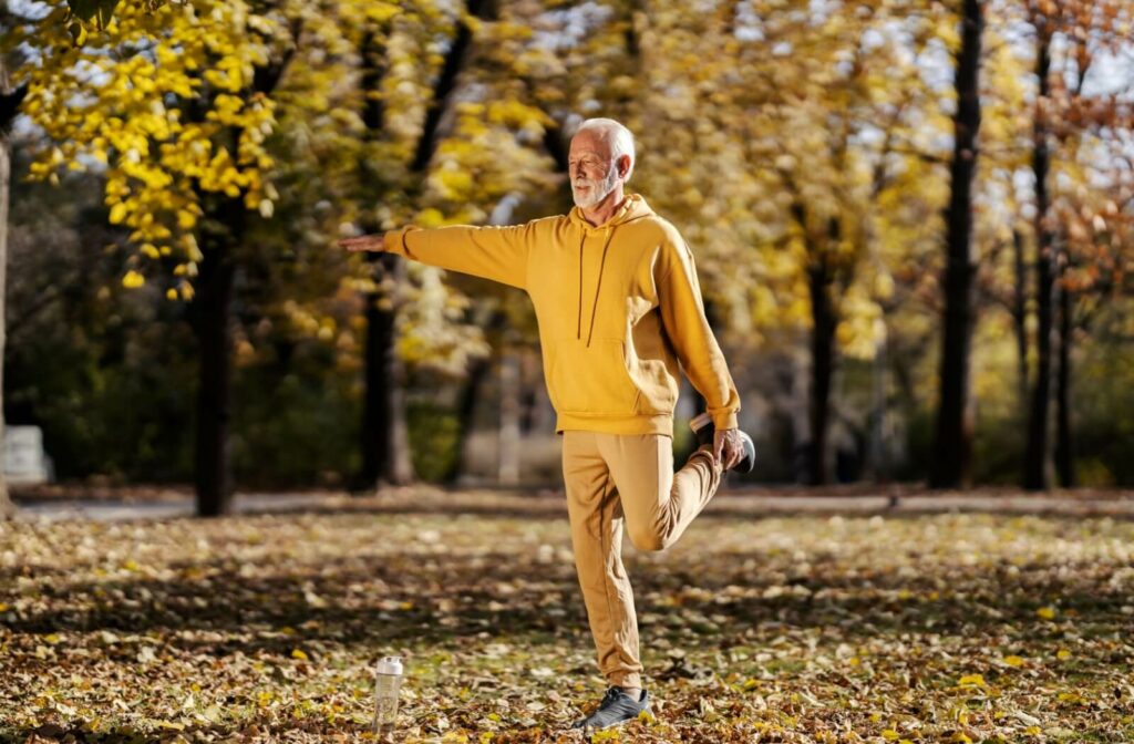 A senior in a yellow sweater stretches out their hamstrings while walking around their senior living community grounds