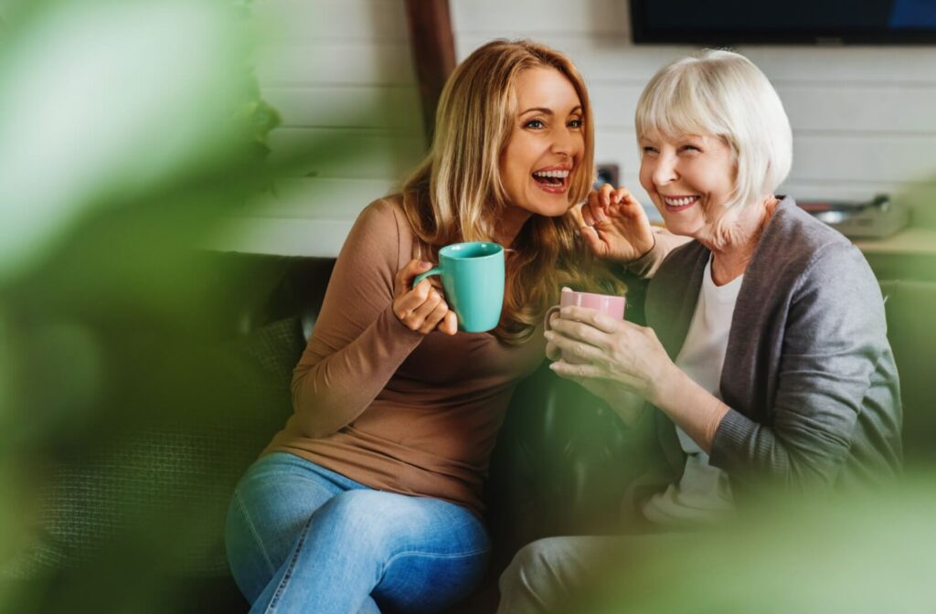 An adult and their senior parent with dementia giggle together over morning tea and light, fun conversation
