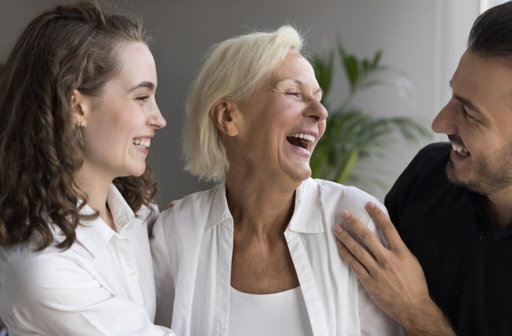 Two adults laugh and lovingly hug their senior parent with dementia, enjoying being present in the moment with each other