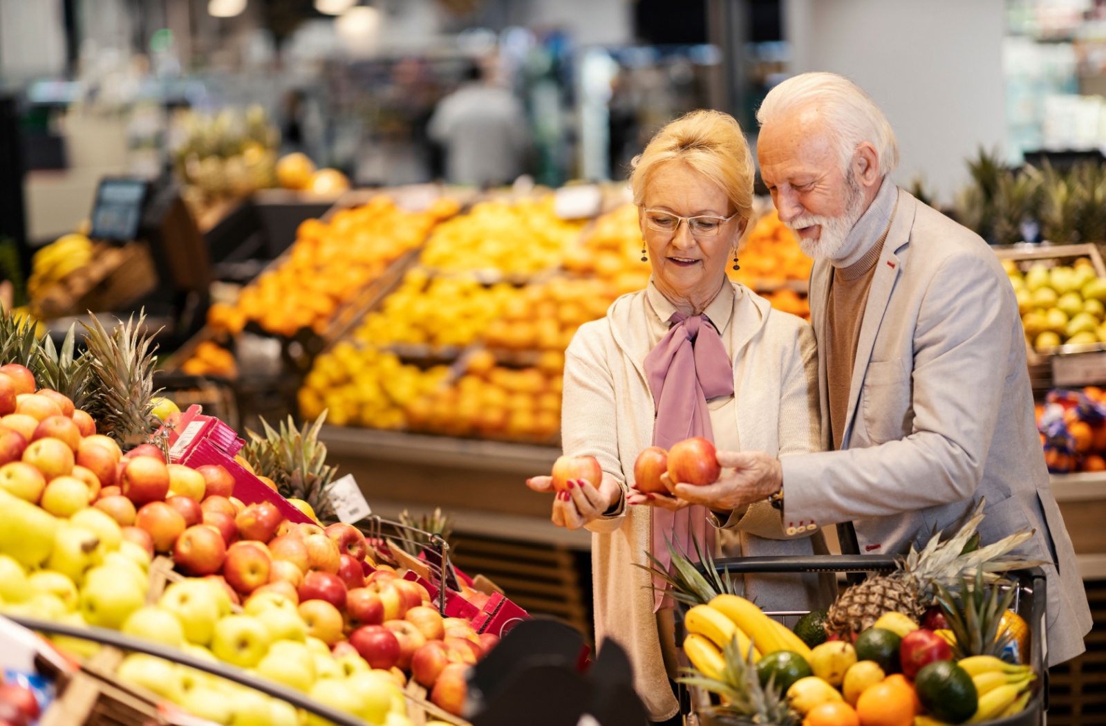 A senior couple at the grocery store weigh the options of different apples while shopping in the fruit section.