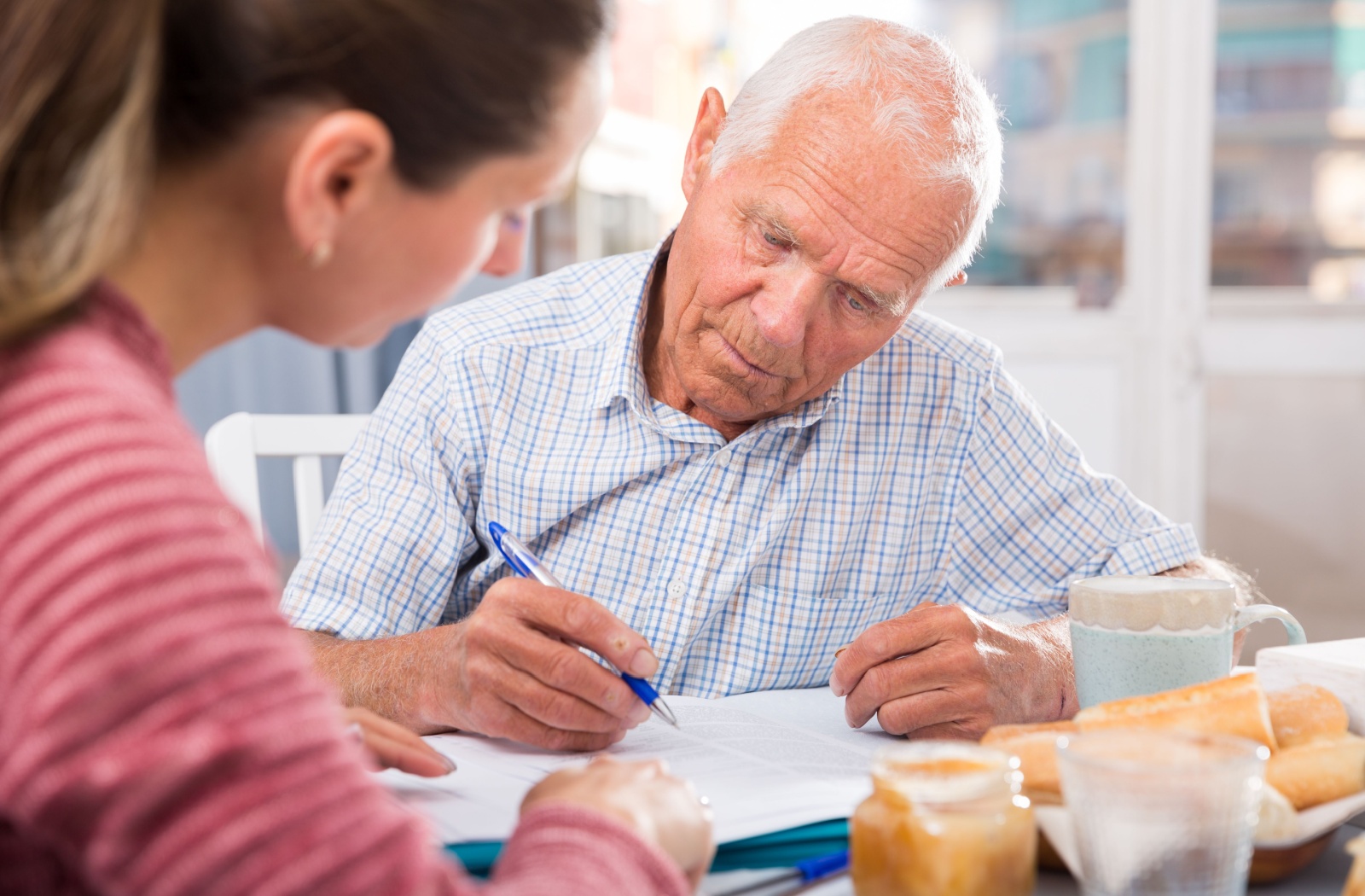 Senior signing a document with the assistance of a caregiver demonstrating cognitive ability.