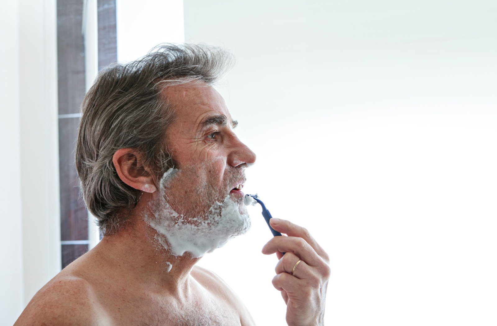 A senior person performing an activity of daily living by shaving their face.