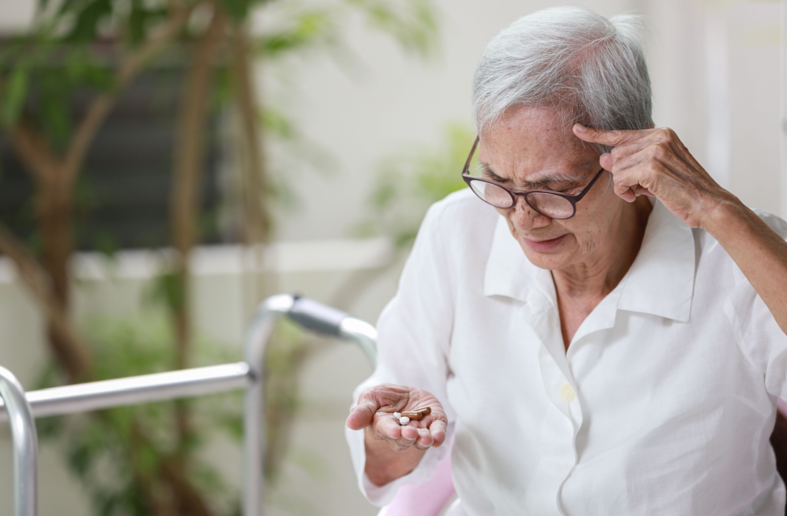 A senior with dementia holds a handful of pills in confusion, trying to remember whether they’ve already taken their dose.