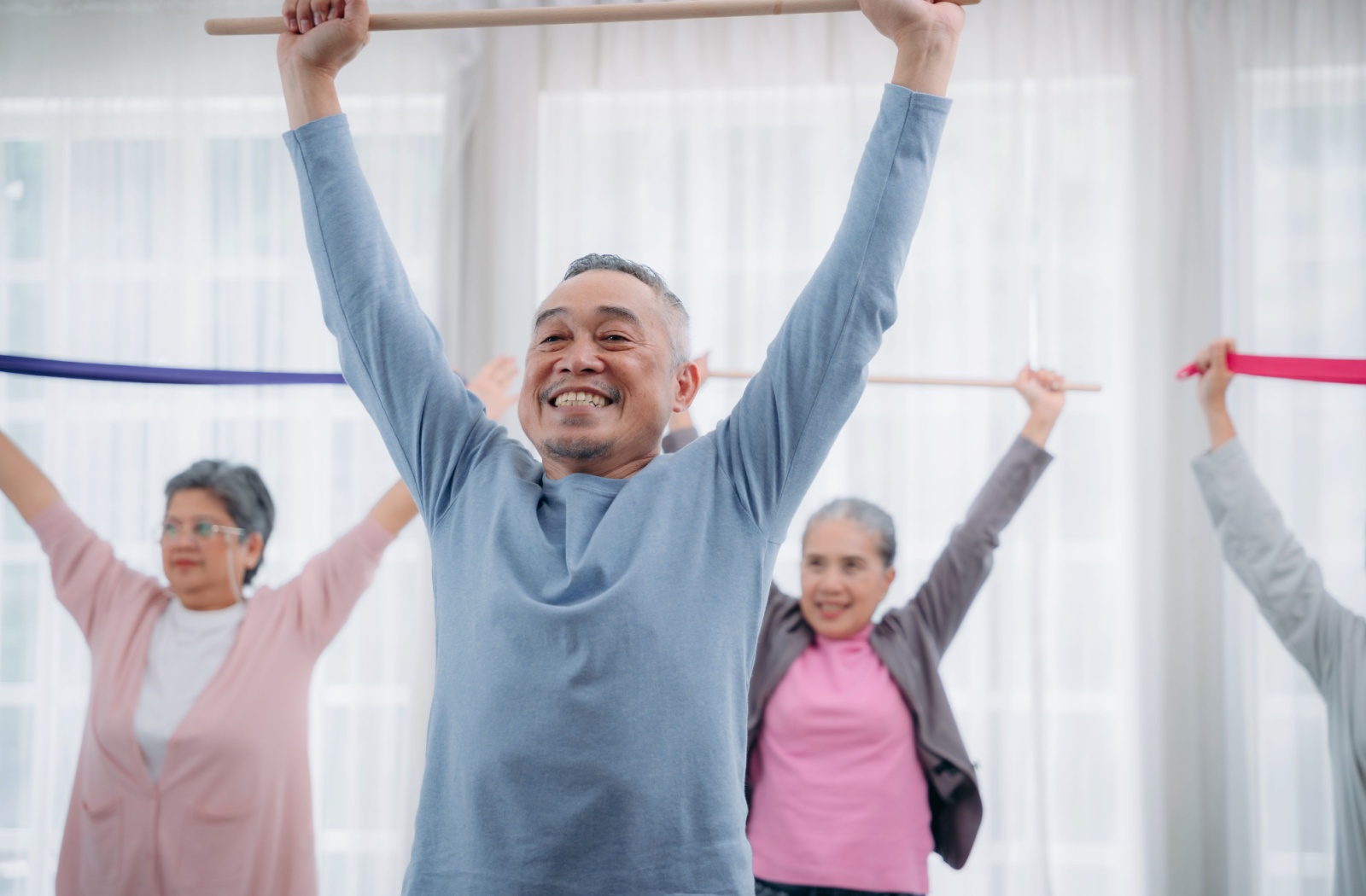 A group of older adults grinning while using overhead resistance bands during an occupational therapy class.