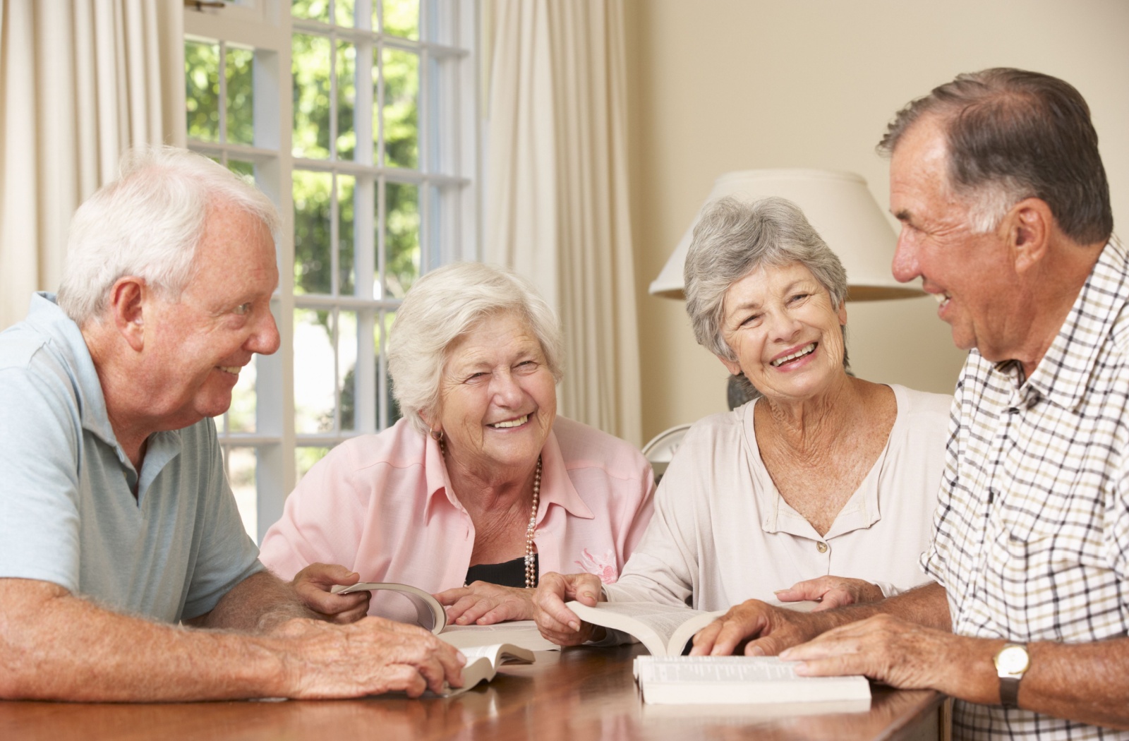 A group of older adults in senior living gathered around a table with novels during their book club.