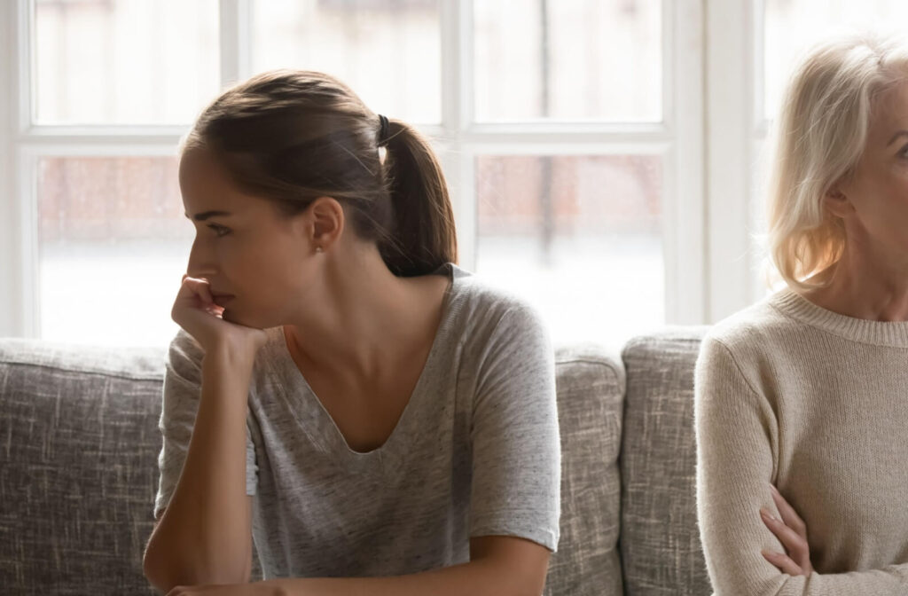 Two people sitting apart on a couch looking away from each other in visible tension or frustration