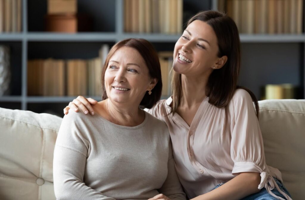 Two people smiling while sitting close on a couch one with an arm around the other showing affection and support