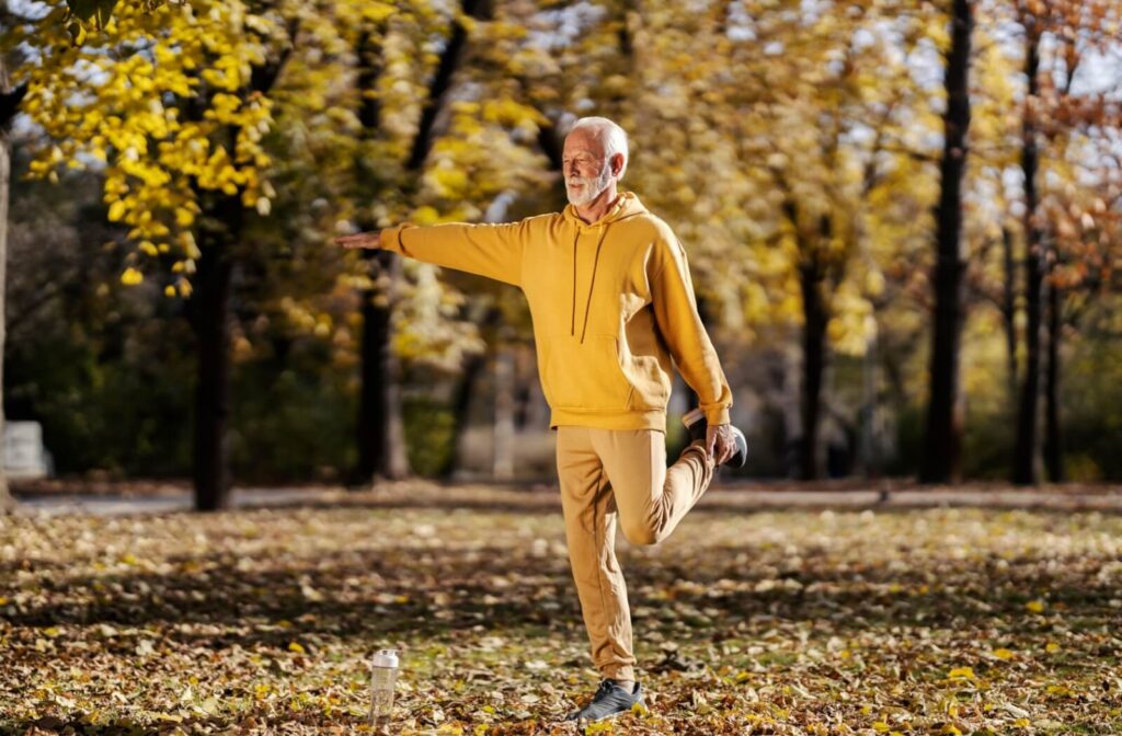 A senior in a yellow sweater stretches out their hamstrings while walking around their senior living community grounds