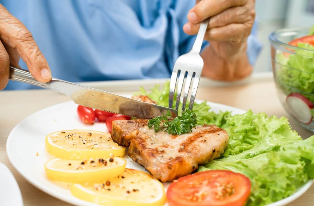A senior cuts into a cooked piece of fish, surrounded by veggies, as a mediterranean-inspired meal