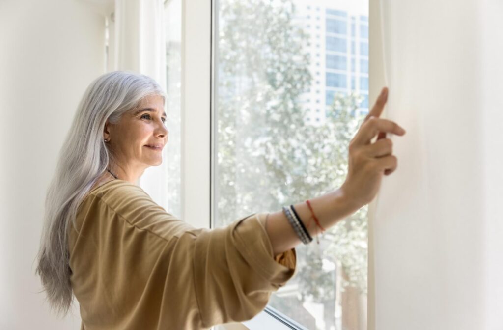 A senior looks out the window after opening their curtains in the morning, excited about the upcoming day in assisted living