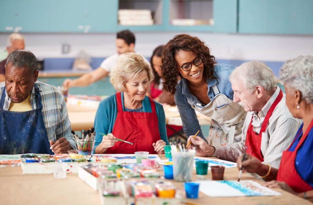 A group of seniors sit together painting during an afternoon class, getting help and advice from an instructor
